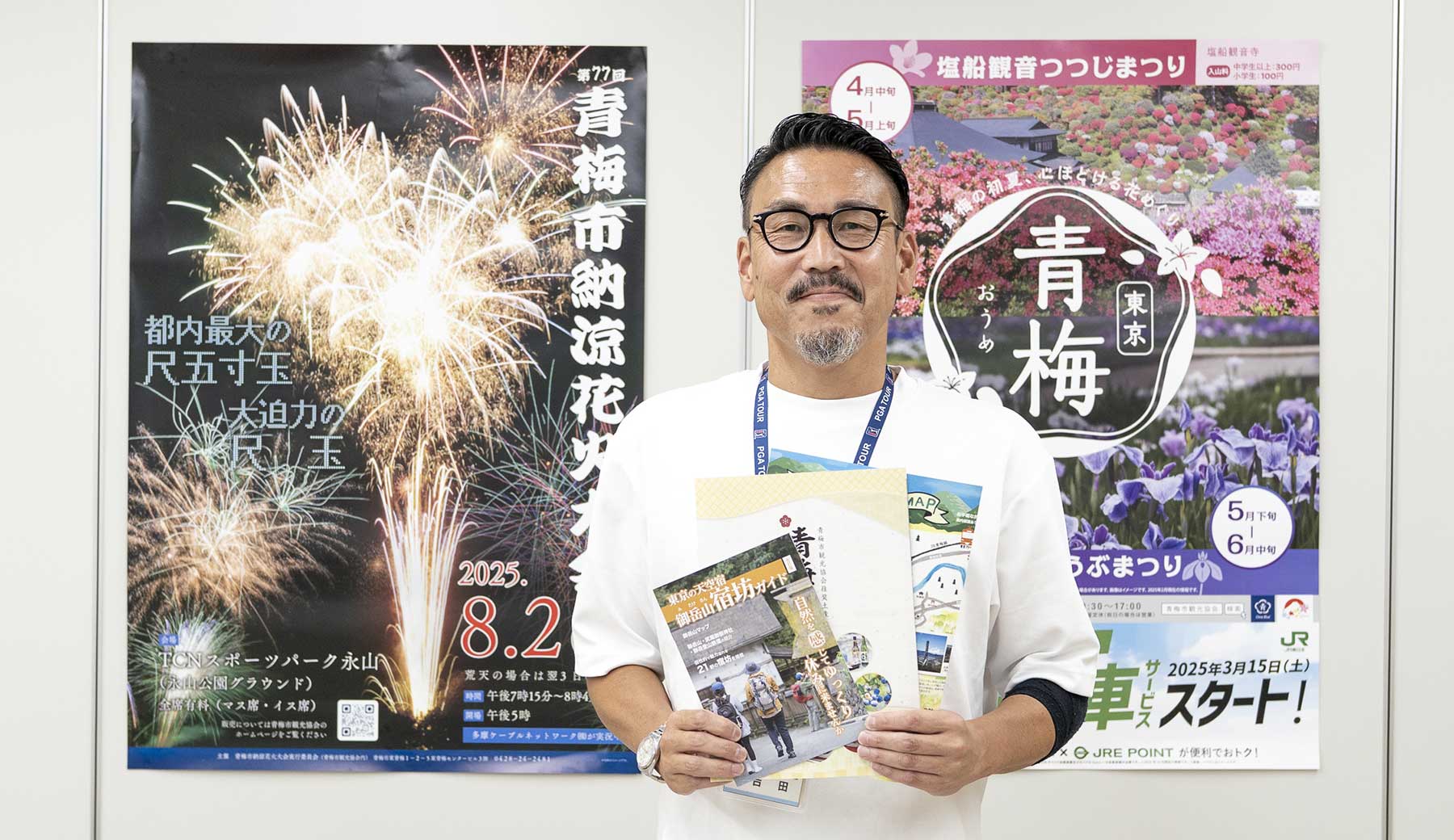 一般社団法人青梅市観光協会の吉田さんが青梅市の観光ポスターの前で観光パンフレットを持った写真
