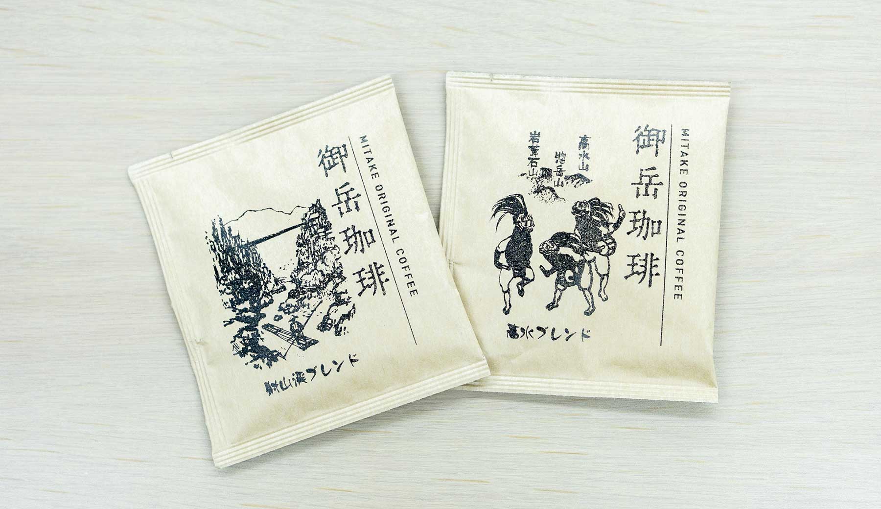 青梅市観光協会が開発した「御岳珈琲」射山渓ブレンドと高水ブレンドのパッケージ。クラフト調の紙パッケージにスタンプで押したようなイラストがプリントされている。