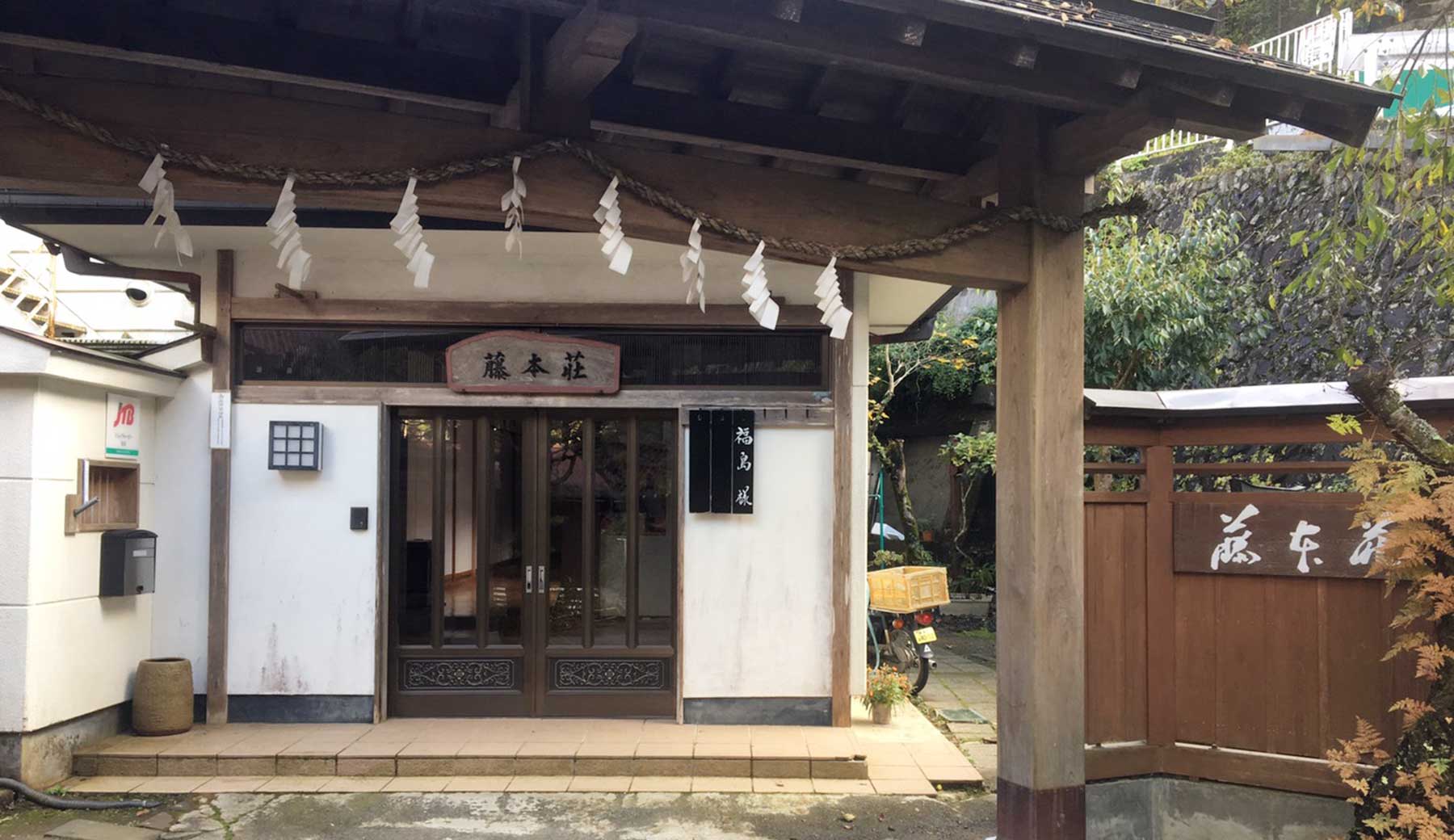 青梅市御岳山の宿坊の入口の写真。屋根付きの門の奥に玄関と看板が見える。昔ながらの旅館のように見えるが、門にはしめ縄が飾られている。