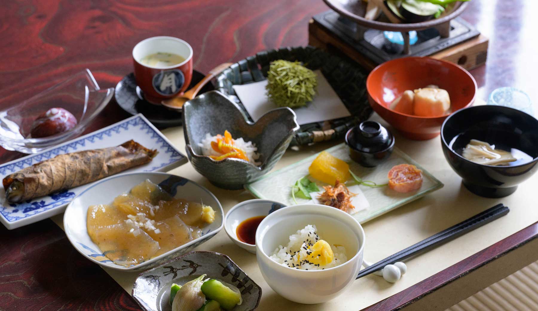 青梅市御岳山の宿坊の食事の写真。前菜の盛り合わせ・朴葉(ほおば)焼き・茶碗蒸し・栗ご飯・刺身こんにゃく・陶板焼きなど10品ほどが並んでいる。