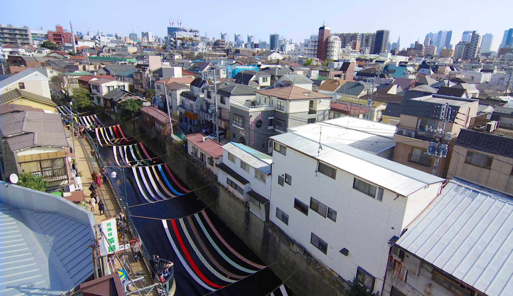 新宿区落合で開催される「染の小道（そめのこみち）」イベントで、妙正寺川に反物がかけられた様子。街中を流れる川面を、何枚ものカラフルな反物が彩っている、