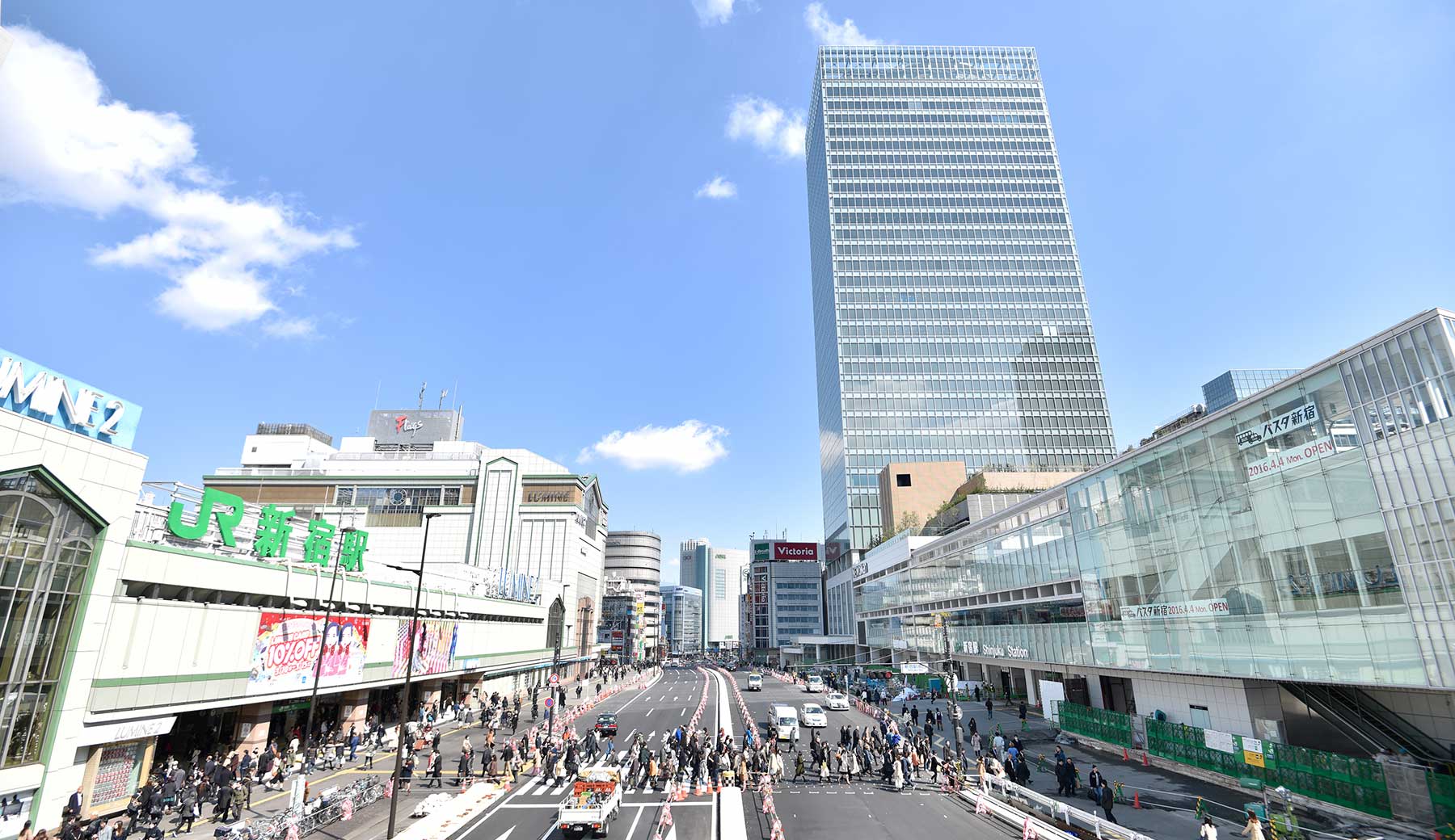 新宿駅南口駅前の甲州街道を新宿御苑方面に向かって撮影した写真。左手にJR新宿駅南口、右手にバスタ新宿があり、広い道路の横断歩道を大勢の人が行き来している。