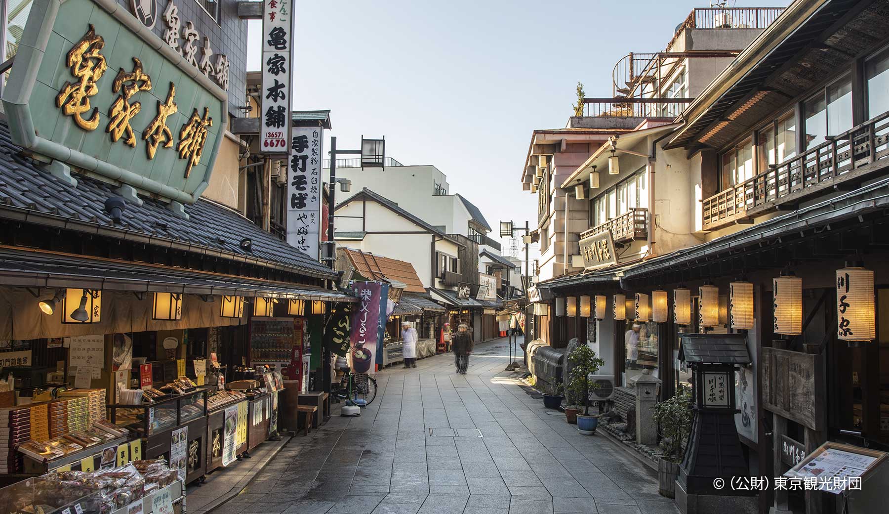 葛飾区の柴又帝釈天参道商店街の風景。重厚感がある看板や提灯が並ぶ店頭で、昔ながらのお団子やうなぎの蒲焼などを販売している。